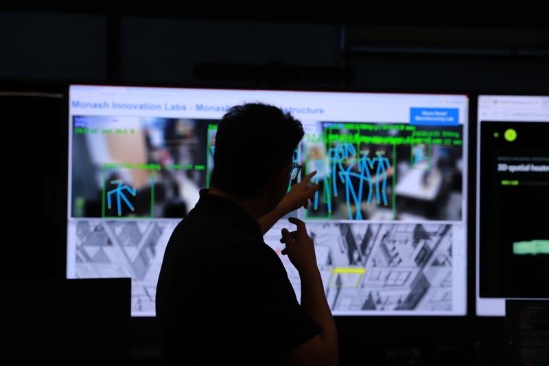 A team member points at live pose-detection output on the lab screens