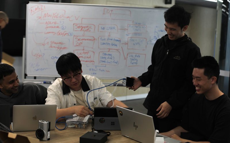 Team members testing the modular platform hardware in front of a whiteboard system diagram
